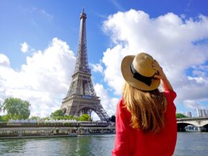 A woman in a hat admiring the Eiffel Tower in Paris on a sunny day, the perfect scene for travelers using rent a car Paris services.