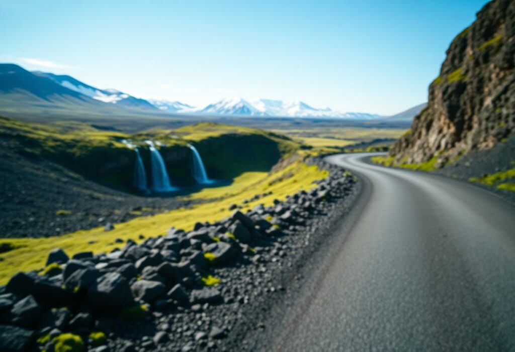 A blurred landscape featuring a winding road on the right, bordered by rocky terrain and green grass. To the left, twin waterfalls cascade into a pool. Snow-capped mountains are visible under a clear blue sky. The image conveys a sense of remote, untouched natural beauty.